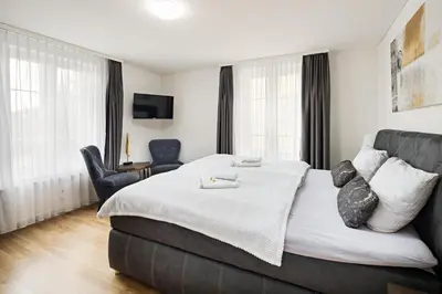 a hotel room with a large bed and a chair at VISIMO Apartments Felsenstrasse St Gallen - Elegant heritage building in a quiet neighbourhood in St. Gallen