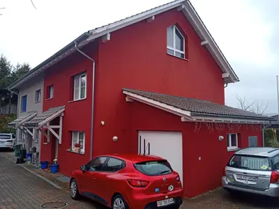 a red house with a red car parked in front of it at B&B Im Bitzi in Zuzwil