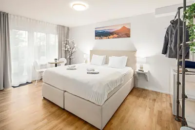 a white bedroom with a large bed and a table at VISIMO Apartments Lehnstrasse St Gallen - Stylish, Smart, Connected in St. Gallen