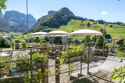 a patio with tables and umbrellas and mountains at Hotel Frohe Aussicht in Weissbad