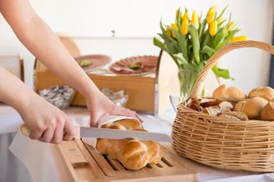 a person cutting bread on a cutting board with a knife at Hotel Metropol in Widnau