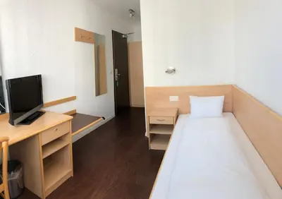 a room with a bed and a desk with a television at Hotel Metropol in Widnau