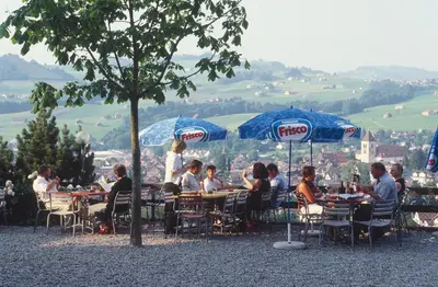a group of people sitting at tables under umbrellas at Panorama Hotel Freudenberg in Appenzell