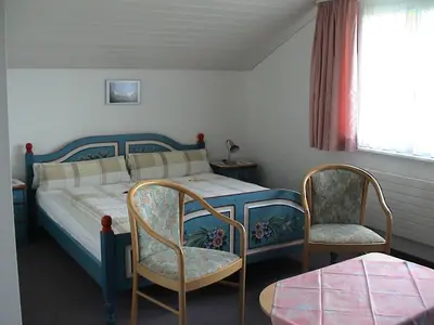 a bedroom with a blue bed and two chairs at Panorama Hotel Freudenberg in Appenzell