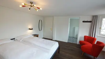 a bedroom with a white bed and a red chair at Alte Metzg - Boutique Pension in Appenzell