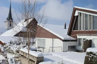 a house with snow on the roof and a church at Hotel Swiss Views in Hemberg