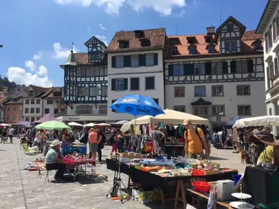 a group of people at an outdoor market with tables and umbrellas at 2 rooms with balcony, central, quiet location in St. Gallen