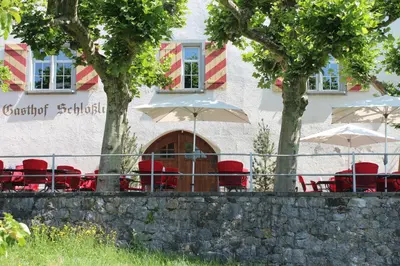 a building with red chairs and umbrellas in front of it at Hotel Restaurant Schlössli Sax in Sax
