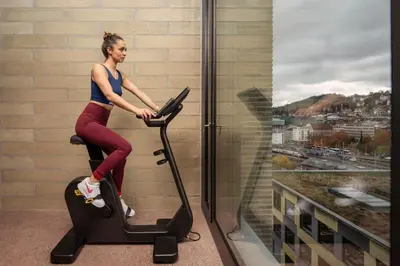 a woman riding on an exercise bike in front of a window at Tailormade Hotel LEO St Gallen in St. Gallen