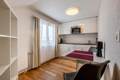 a white bedroom with a bed and a kitchen at Aparthotel Mama Home Stankt Georgen in St. Gallen