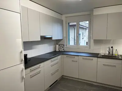 a white kitchen with white cabinets and a window at Charmante und zentrale Wohnung am Weiherpark Arbon in Arbon